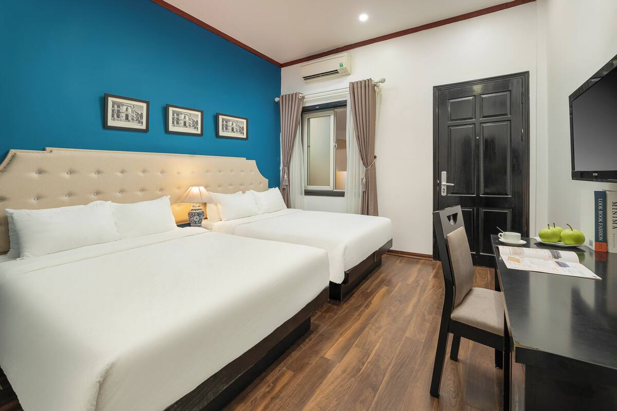 Une chambre d’hôtel avec deux lits, un bureau, une chaise, une télévision et une fenêtre avec des rideaux.