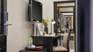 Habitación de hotel con escritorio, televisor de pantalla plana, un florero con flores, lámpara y una silla.