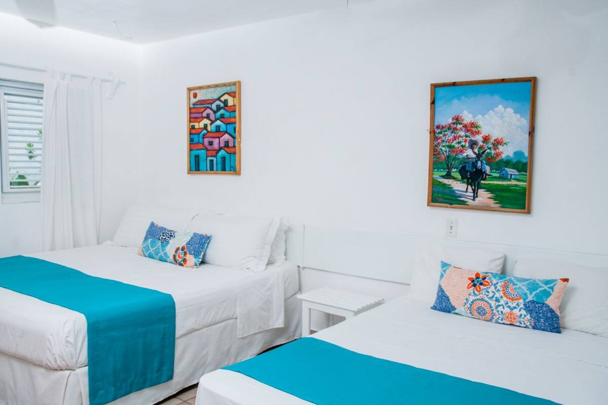 Ein Hotelzimmer mit zwei Betten, weißer Bettwäsche und farbenfrohen Bildern an den Wänden.
