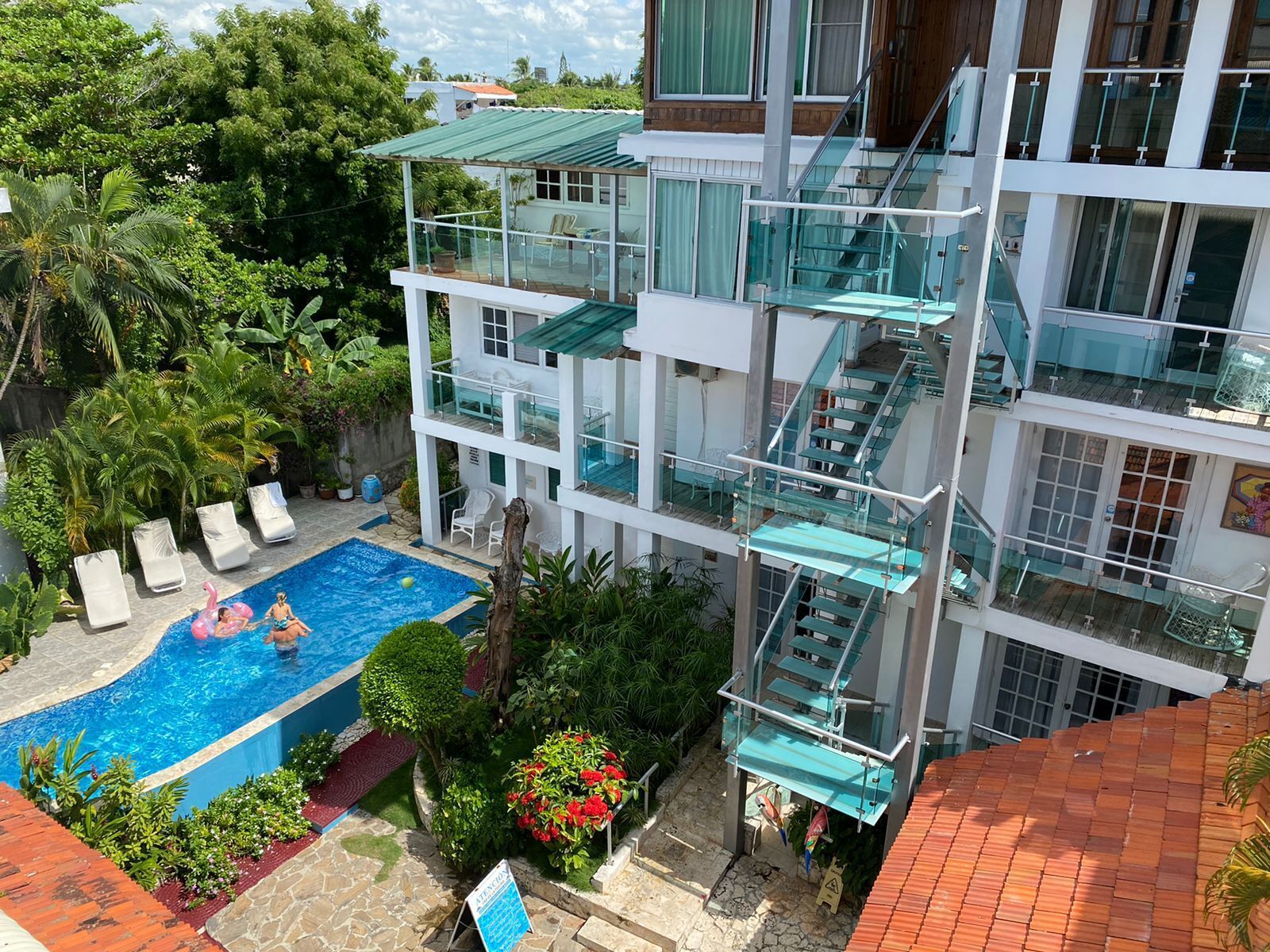 A multi-story hotel with a rooftop pool, glass railings, and lush greenery.