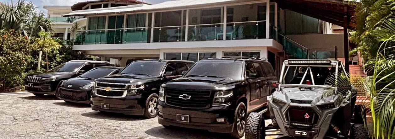 A modern building with a glass facade and a parking area with several SUVs and a 4x4 vehicle.