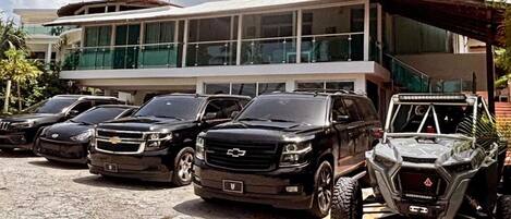 A modern building with a glass facade and a parking area with several SUVs and a 4x4 vehicle.