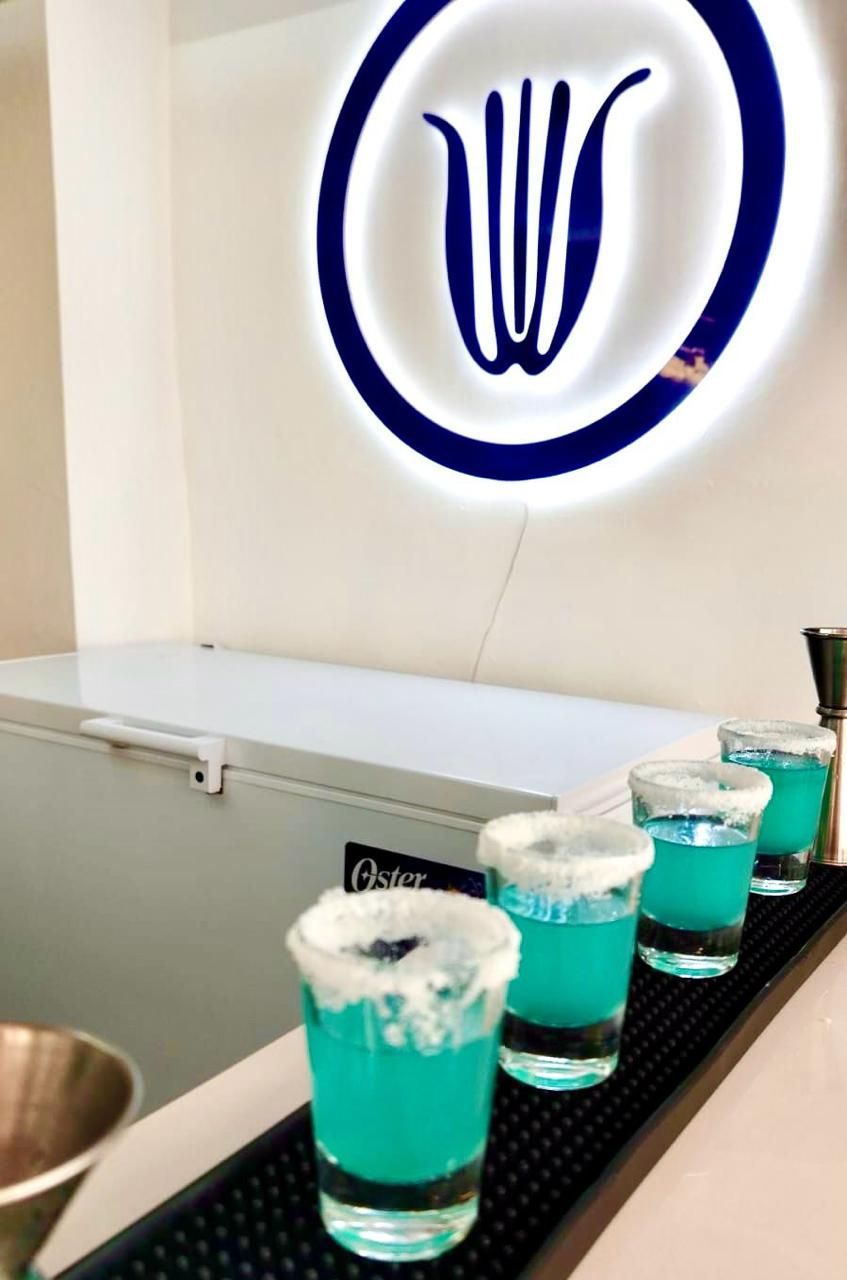A bar area with a neon sign, a bar counter, and shot glasses filled with a blue liquid.