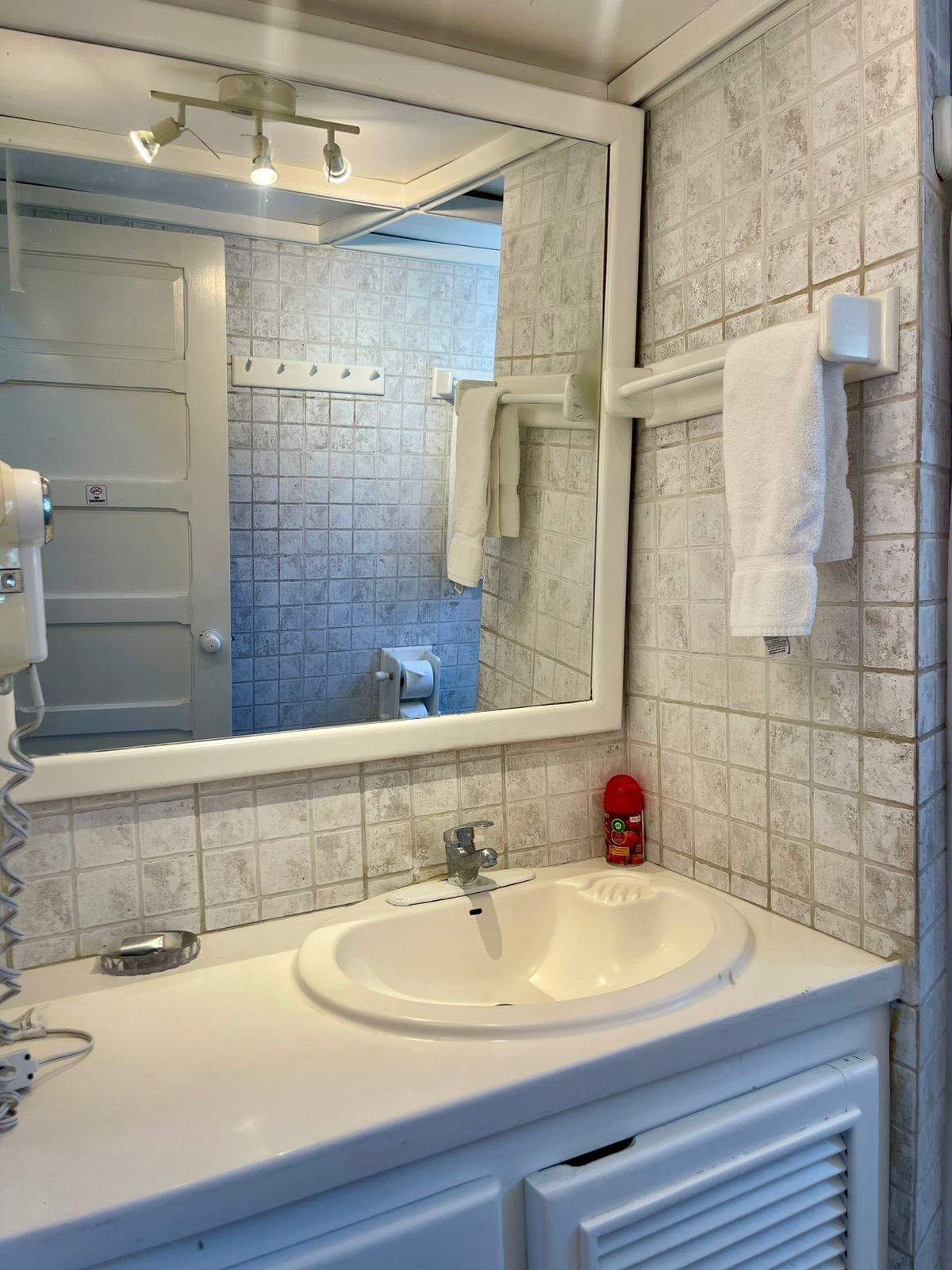 Un baño con un lavamanos blanco, un espejo, un perchero para toallas y un dispensador de papel higiénico.