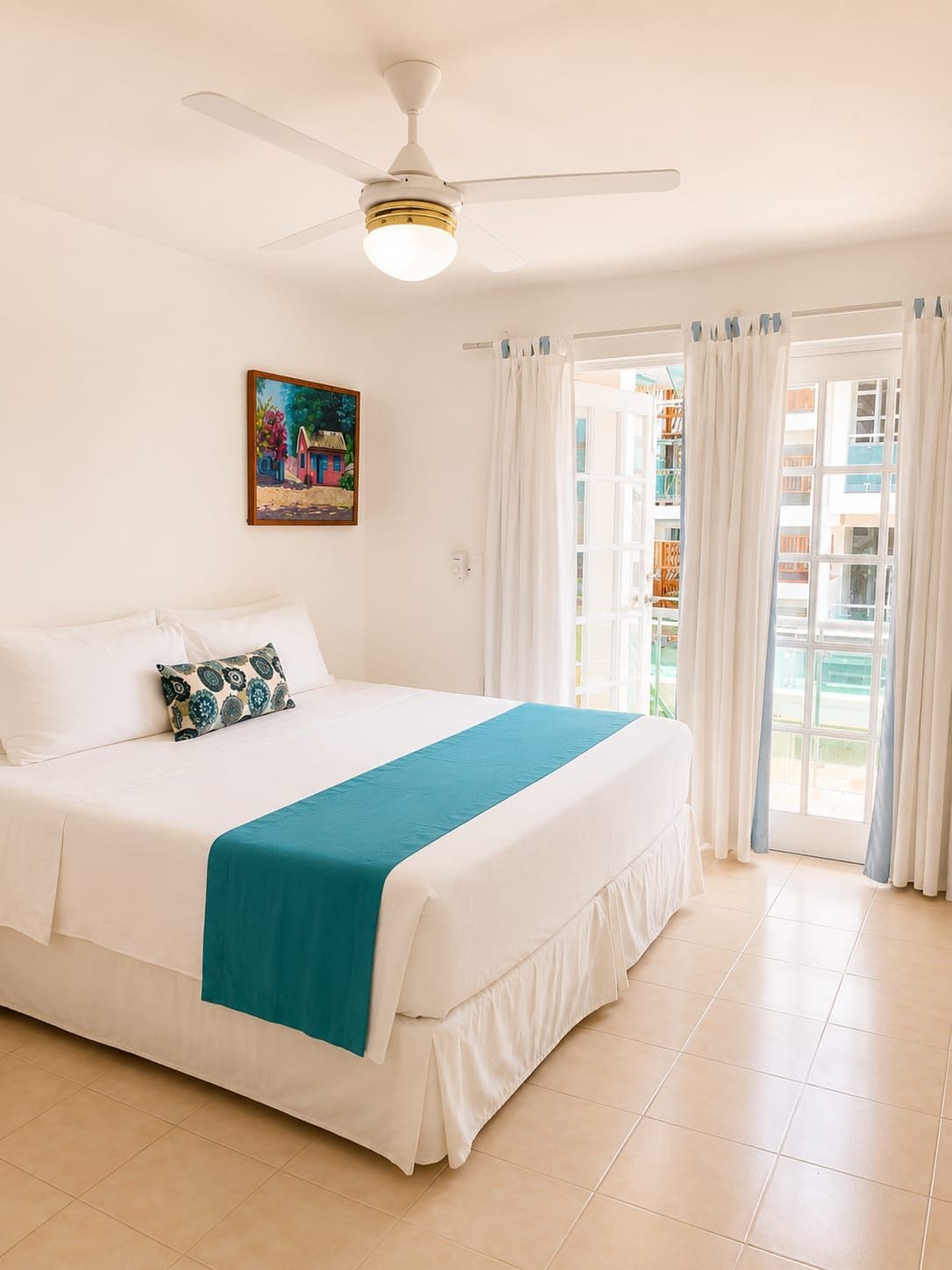 Habitación de hotel con cama, ventilador de techo, un cuadro en la pared y vistas al exterior.