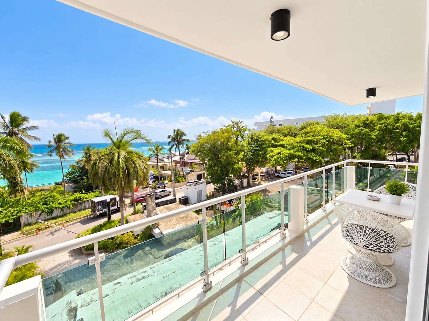 Un balcon offrant une vue dégagée sur l’océan, les palmiers et la rue en contrebas.