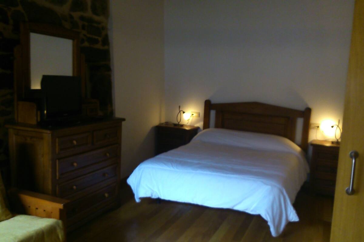 A bedroom with a wooden bed, two bedside tables with lamps, a dresser, and a mirror on the wall.