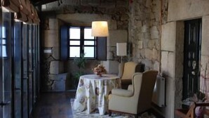 A rustic room with stone walls, wooden beams, a table with a floral tablecloth, and a sofa. - Casa Grande de Cristosende (A Teixeira)