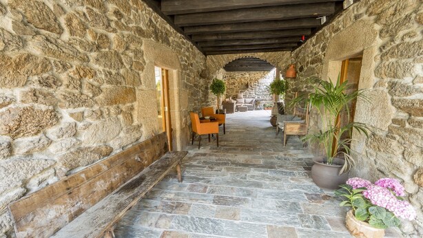 A stone-walled corridor with a wooden bench, potted plants, and a seating area with cushions. - Casa Grande de Cristosende (A Teixeira)