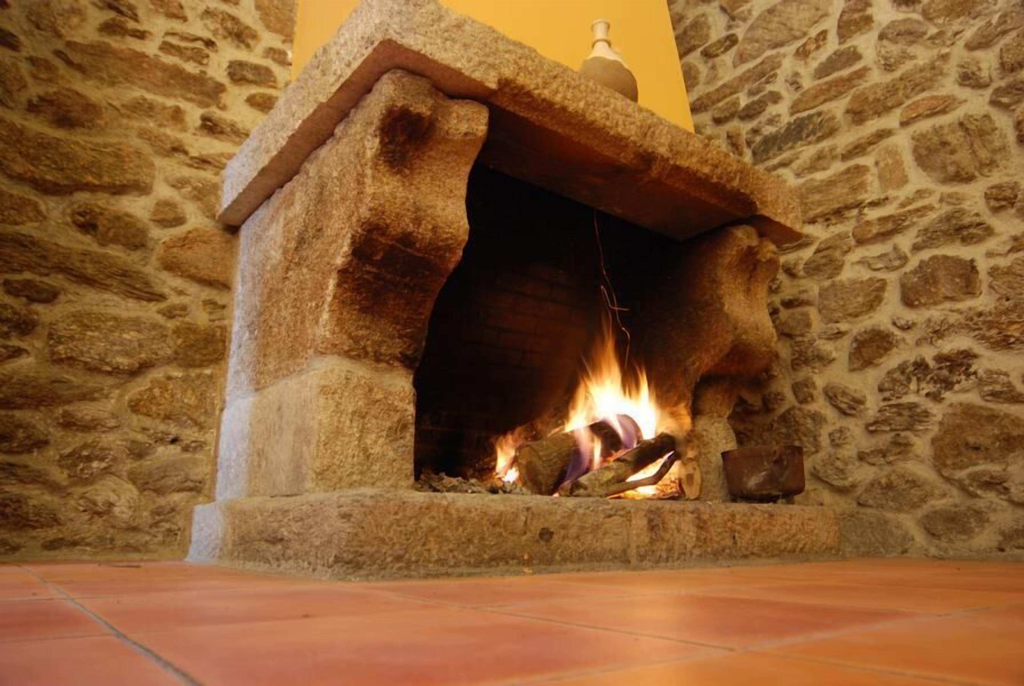 A stone fireplace with a fire burning inside, set against a stone wall.