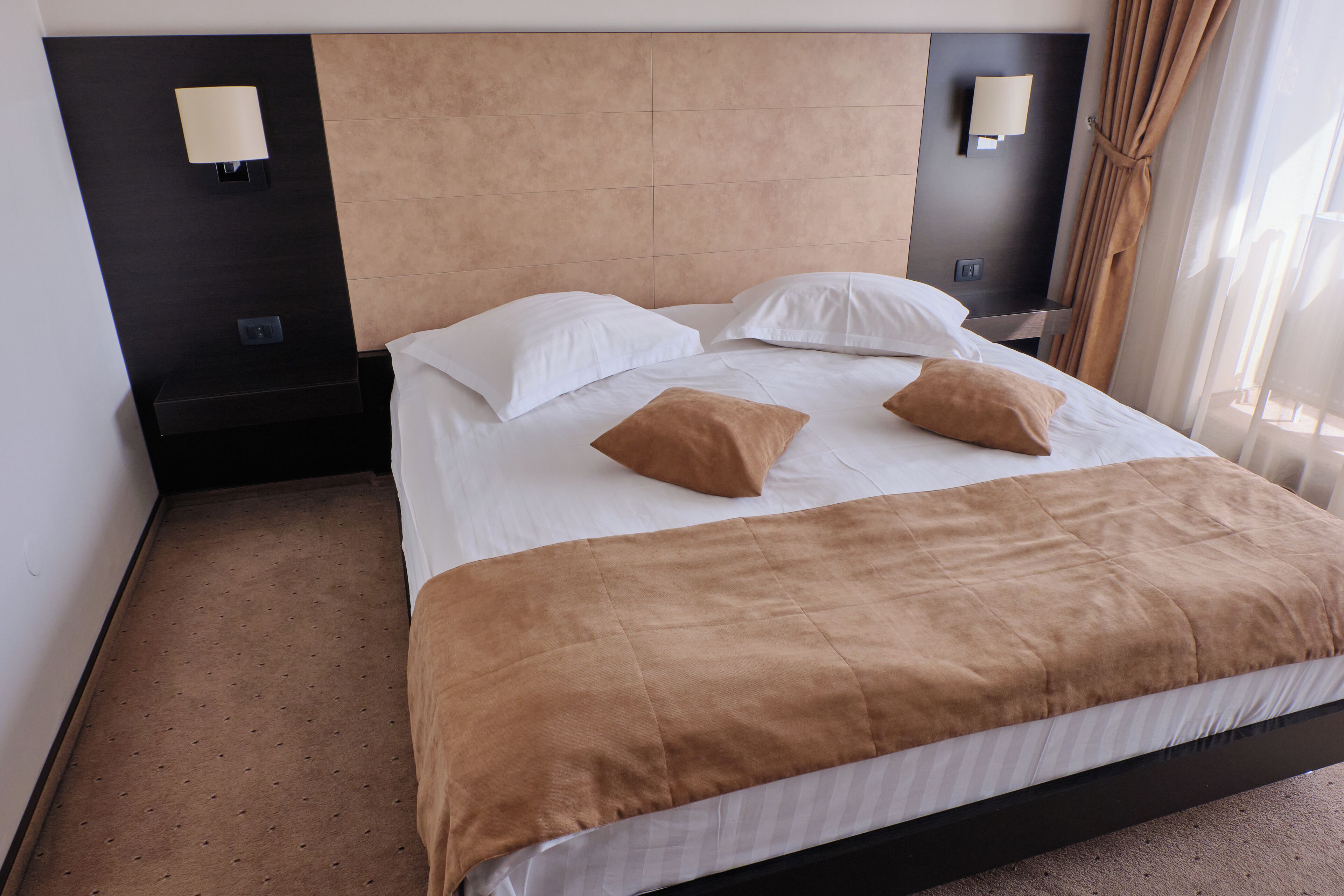 Ein Hotelzimmer mit einem Bett, zwei Wandleuchten und einem Fenster mit Vorhängen.