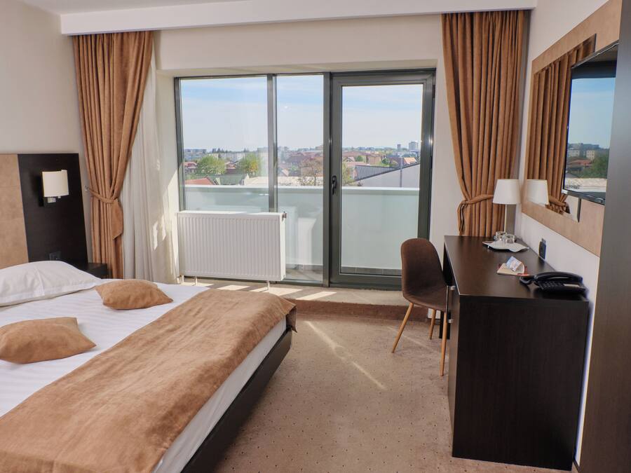 Une chambre d’hôtel avec un lit, un bureau, une chaise, une grande fenêtre donnant sur un beau paysage et un radiateur.