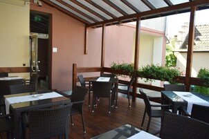 Un espace extérieur aménagé en terrasse, avec des tables et des chaises, une plateforme en bois et une vue sur les bâtiments environnants.