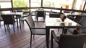 An outdoor patio area with wicker furniture and glass-top tables, featuring a view of buildings and greenery.