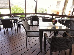 Un espace extérieur aménagé en terrasse, avec des meubles en osier et des tables à plateaux en verre, offrant une vue sur les bâtiments et la verdure.