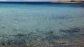 Una spiaggia limpida con acque basse, una barca all'orizzonte e un terreno roccioso sullo sfondo.