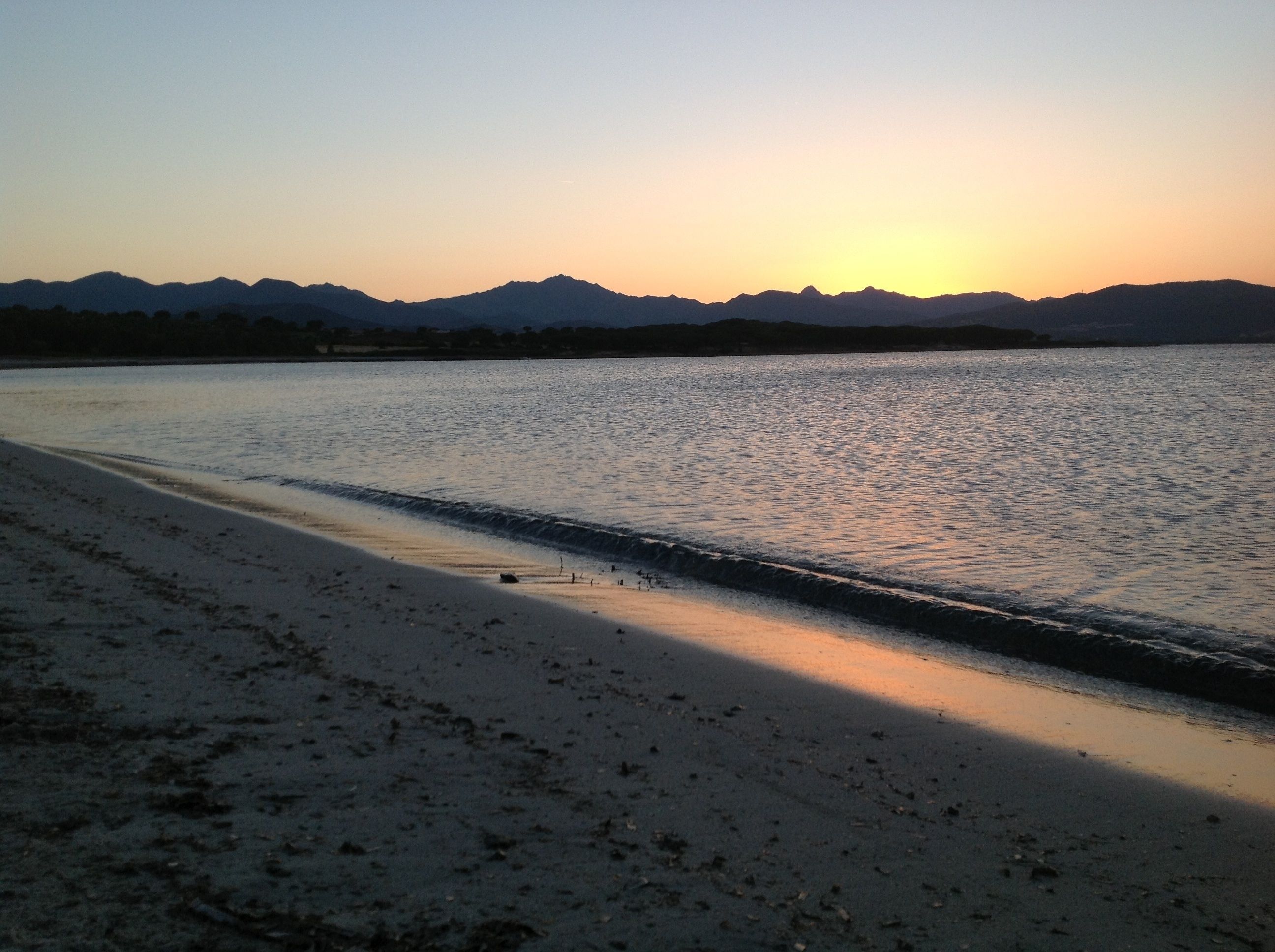 A beach with a calm sea, a clear sky, and distant mountains.