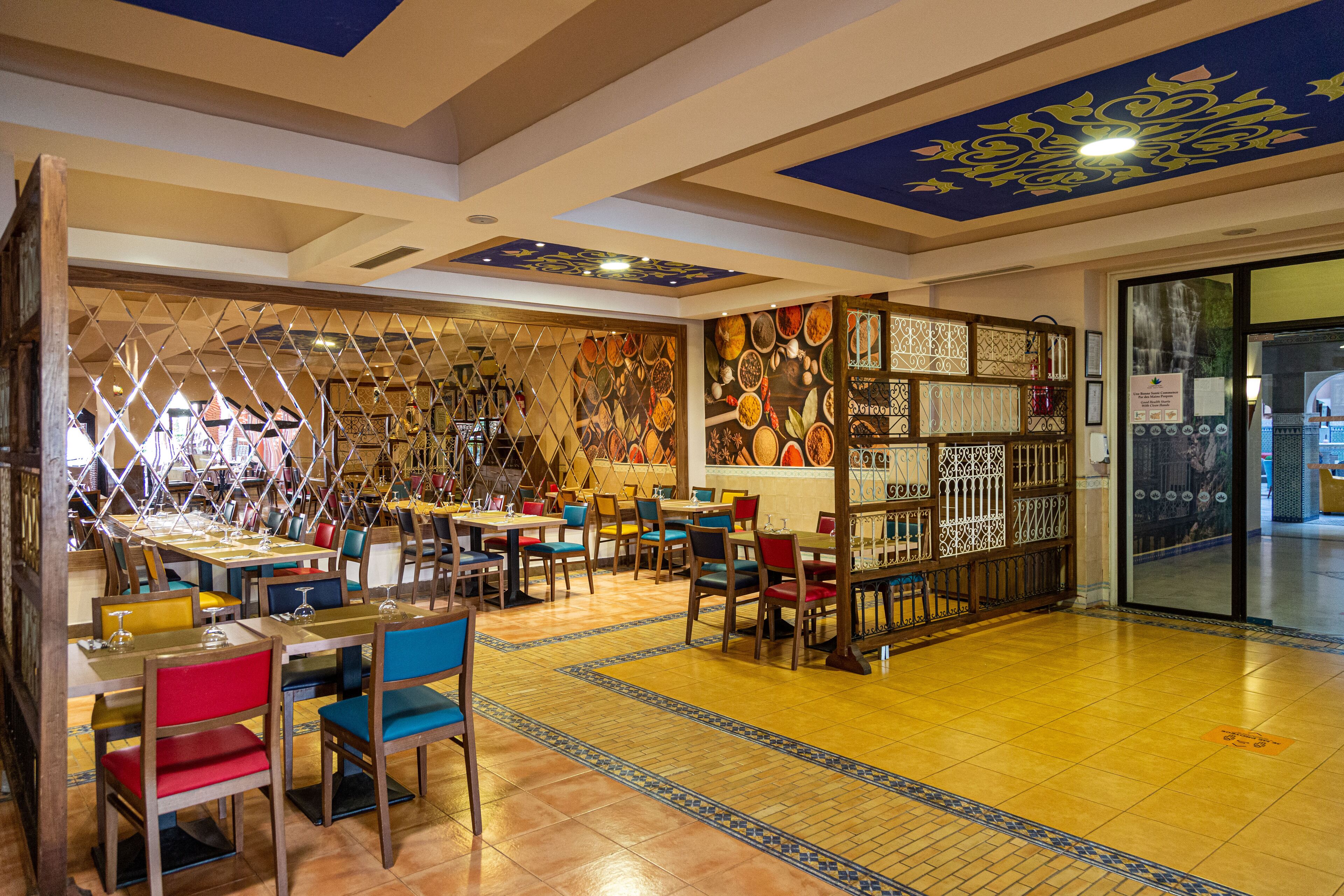 Interior de restaurante con varias mesas y sillas, piso con diseño y decoración artística en el techo.