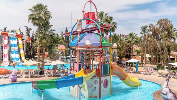 Een waterpark met een centraal zwembad, glijbanen en palmbomen.