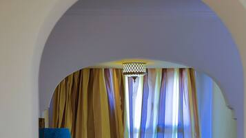 A cozy room with a sofa, a small table, and a lamp. There is a window with curtains and a view of the outside.