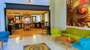 Een hotel lobby met een zwart-wit geruit vloerkleed, een bar en een groene bank.