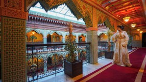 An ornate interior with intricate tile work, a red carpet, and a potted plant.