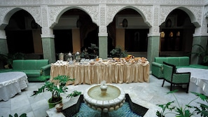 A courtyard with a dining table set for breakfast, surrounded by green cushioned seating and a fountain.