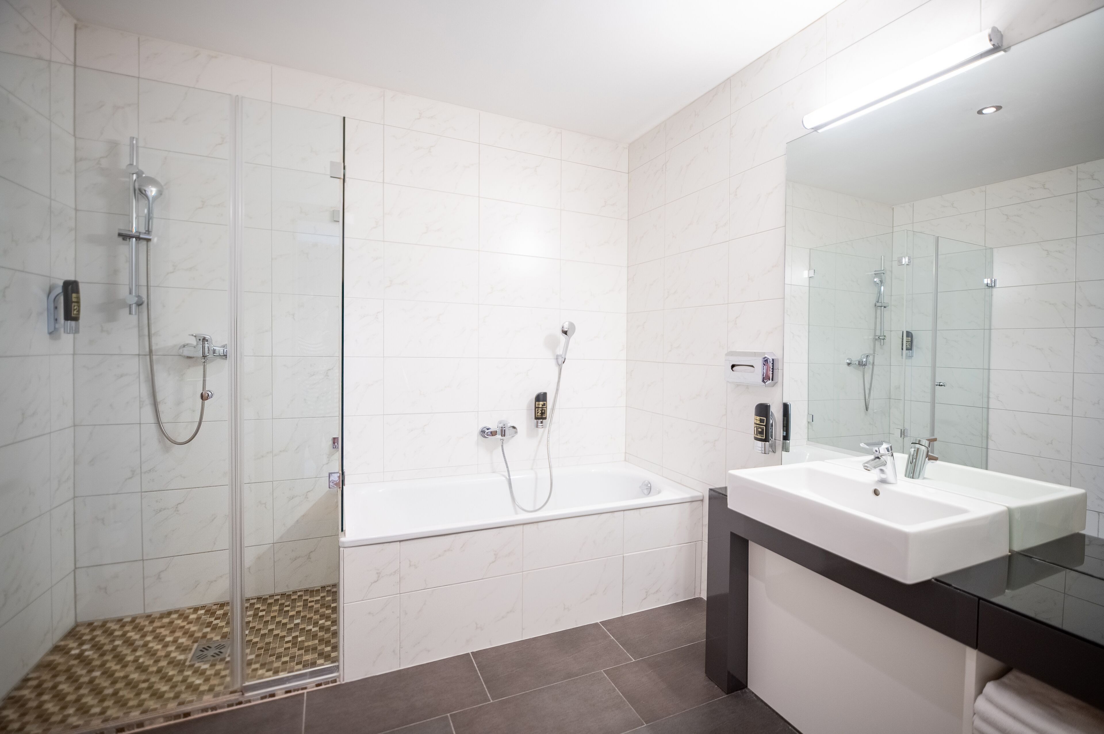 Un baño moderno con ducha de vidrio, bañera independiente y un espejo grande sobre un lavabo blanco.