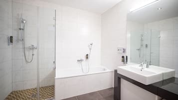 Een moderne badkamer met een douchecabine van glas, een vrijstaand bad en een grote spiegel boven een wit wastafel.