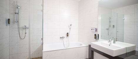 Un baño moderno con ducha de vidrio, bañera independiente y un espejo grande sobre un lavabo blanco.