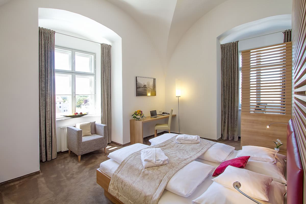 Una habitación de hotel con cama, escritorio, silla y ventana con cortinas.