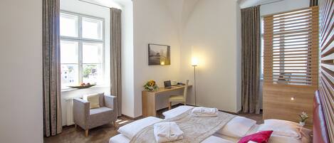 Una habitación de hotel con cama, escritorio, silla y ventana con cortinas.