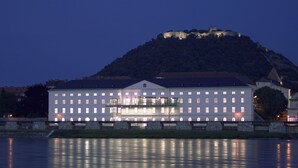 Un grand bâtiment illuminé, doté d’une façade symétrique et de nombreuses fenêtres, situé au bord d’une étendue d’eau calme.
