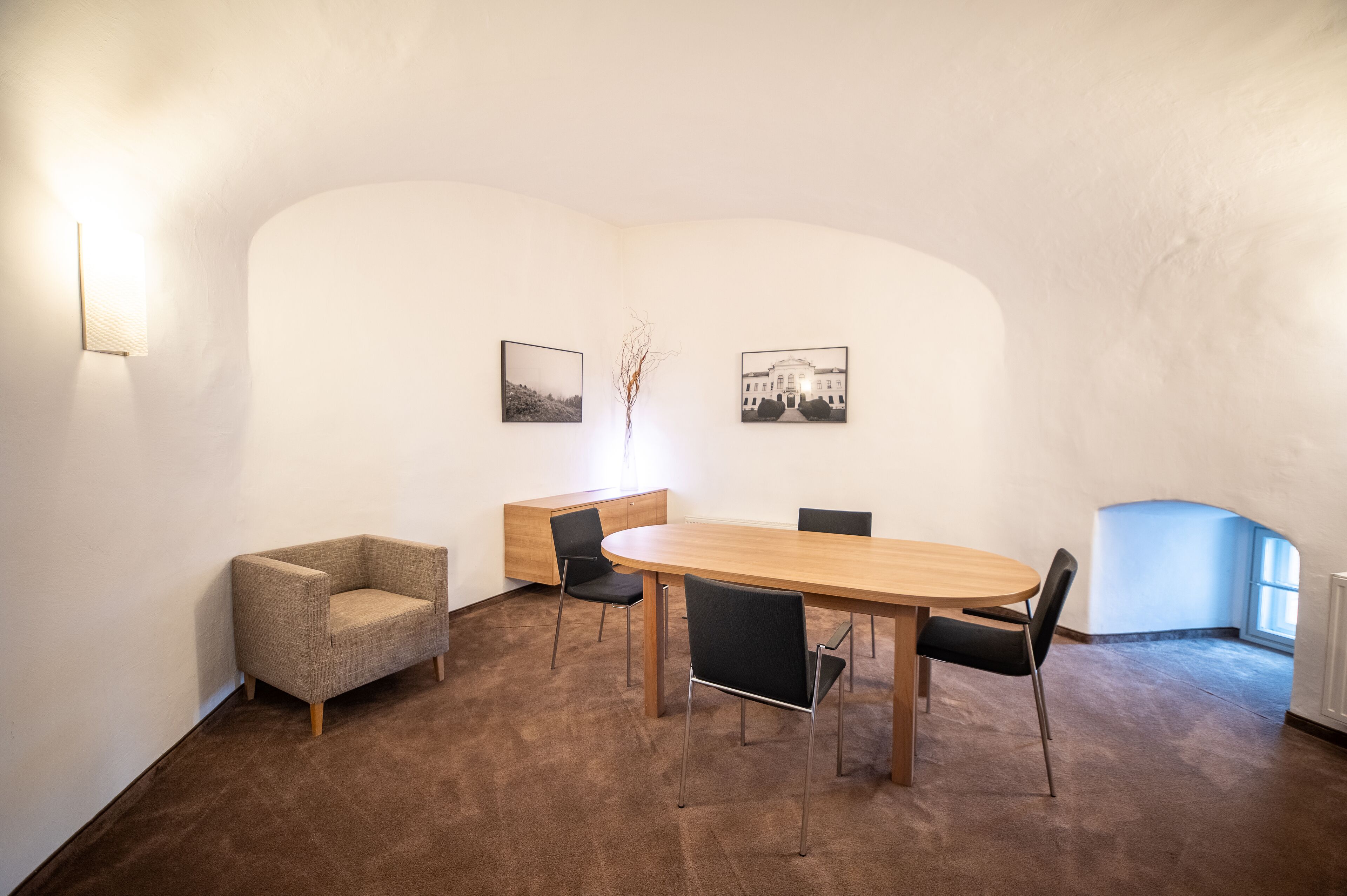 A conference room with a long table, four chairs, a small sofa, and two framed pictures on the wall.