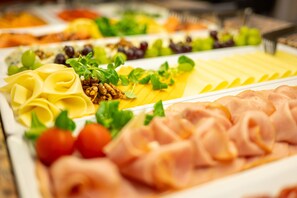 Een buffet met diverse gerechten, zoals pasta, kaas, vleeswaren en garneringen.
