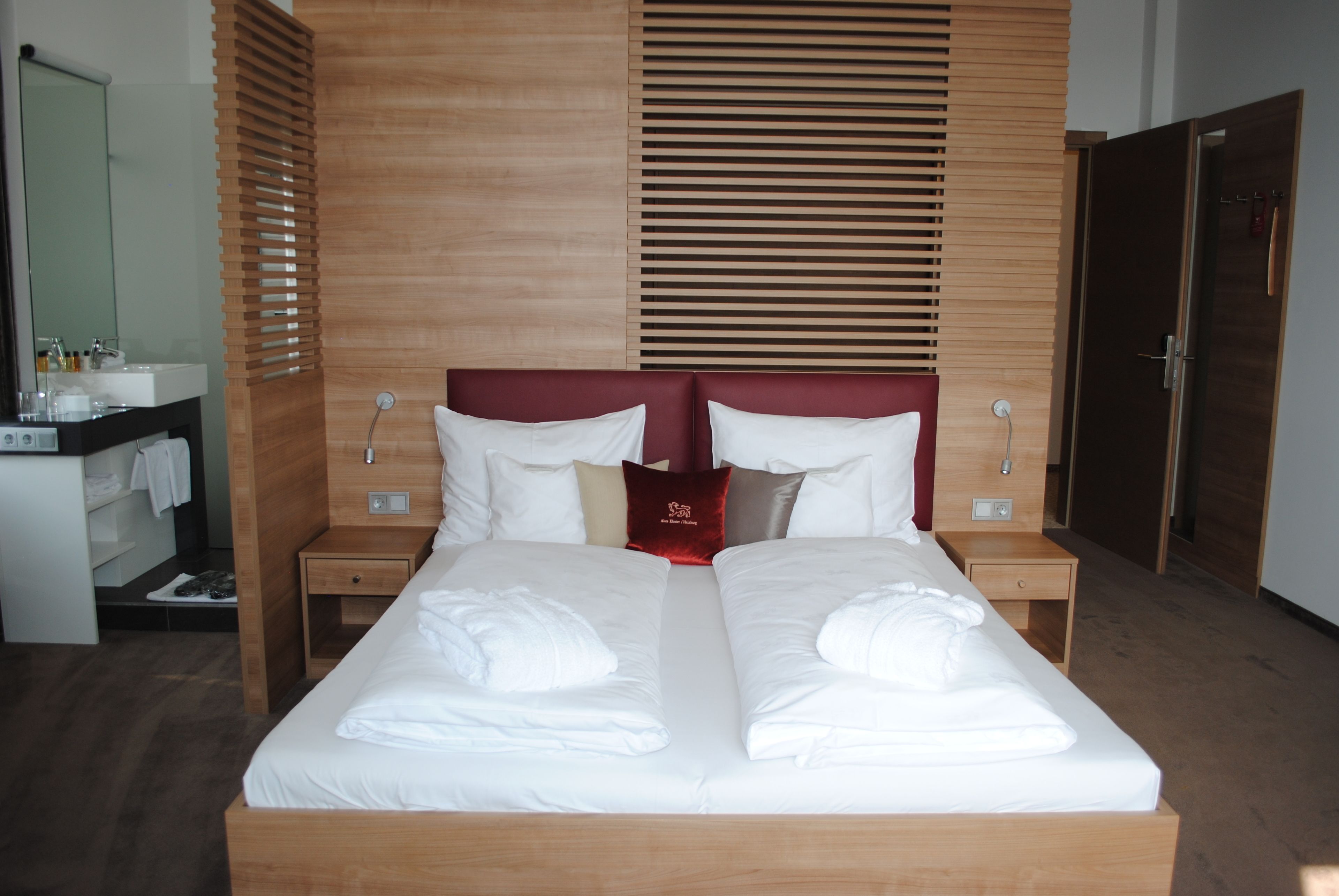 Ein Hotelzimmer mit einem großen Bett, einem Holzkopfstück, zwei Nachttischen, einem Spiegel und einem Kleiderschrank.