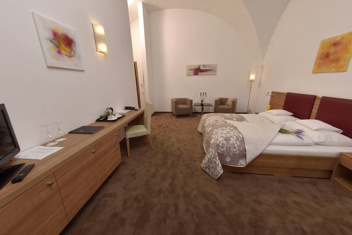 Una habitación de hotel moderna con un escritorio de madera, una cama con colcha estampada floral y dos sillones.