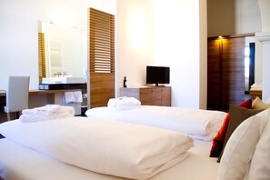 Een hotelkamer met twee bedden, een televisie, een houten garderobe en een badkamer met spiegel en handdoekhouder.