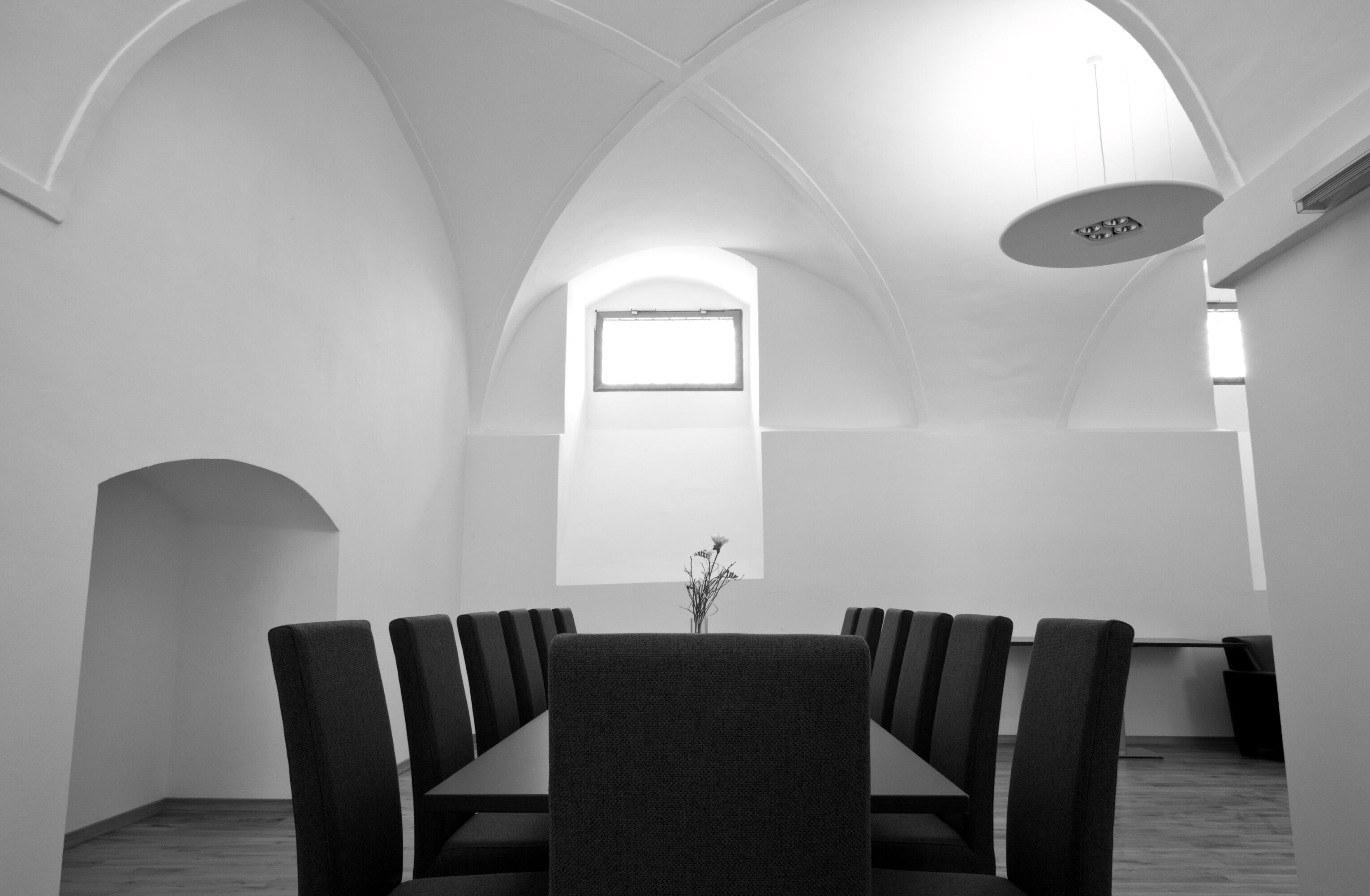 A conference room with a long table and chairs, arched ceiling, and a small window.
