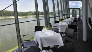 Un restaurant dont les tables sont dressées pour le service, avec vue sur une rivière.