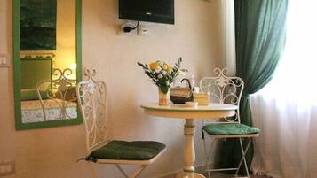 A small room with a single table and two chairs, a television mounted on the wall, and a window with curtains.
