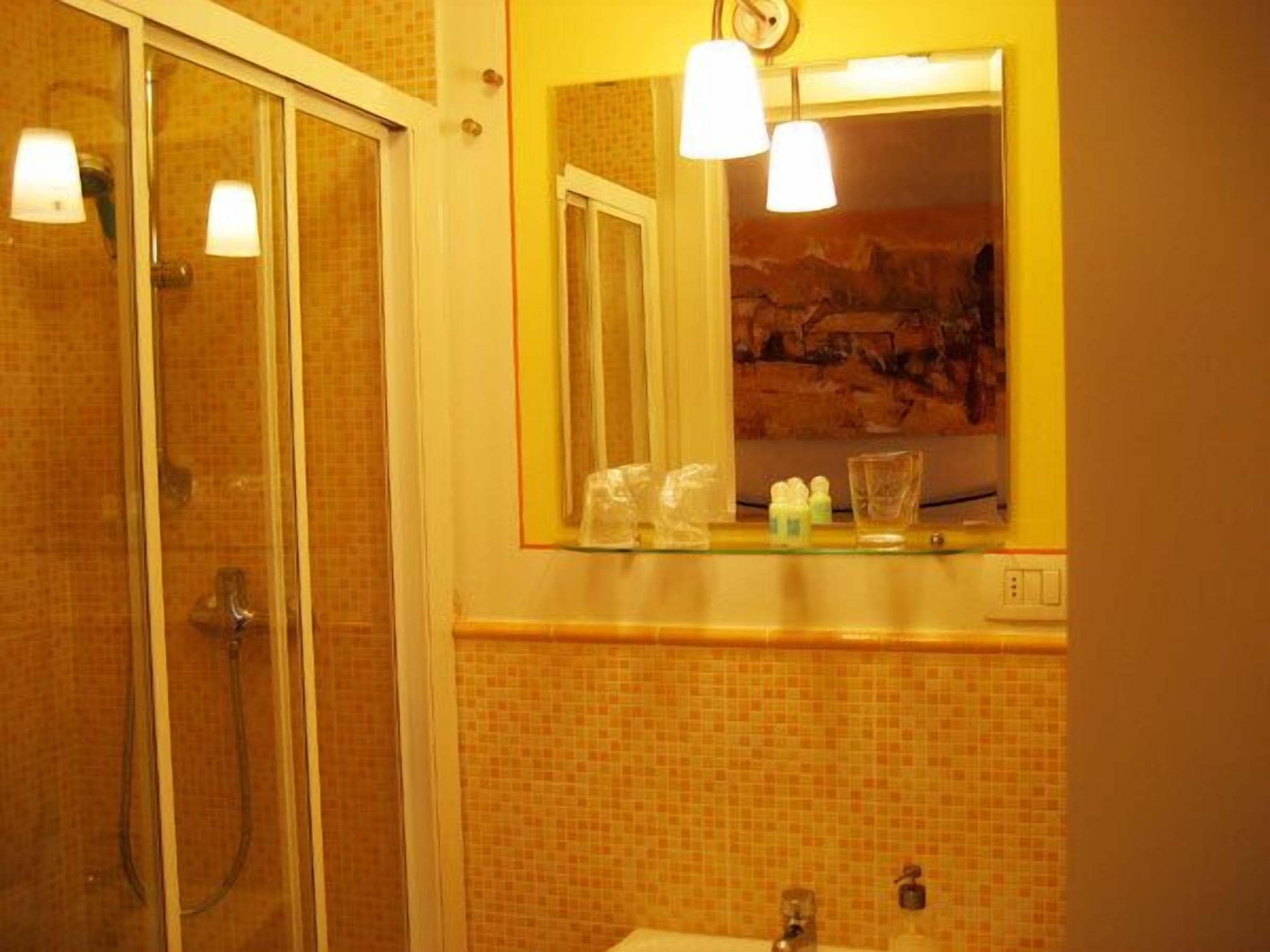 Ein Badezimmer mit Duschkabine aus Glas, Waschbecken mit Spiegel darüber und Toilettenartikeln auf der Ablagefläche.