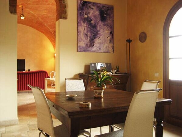 A dining area with a wooden table, chairs, a potted plant, and a painting on the wall.