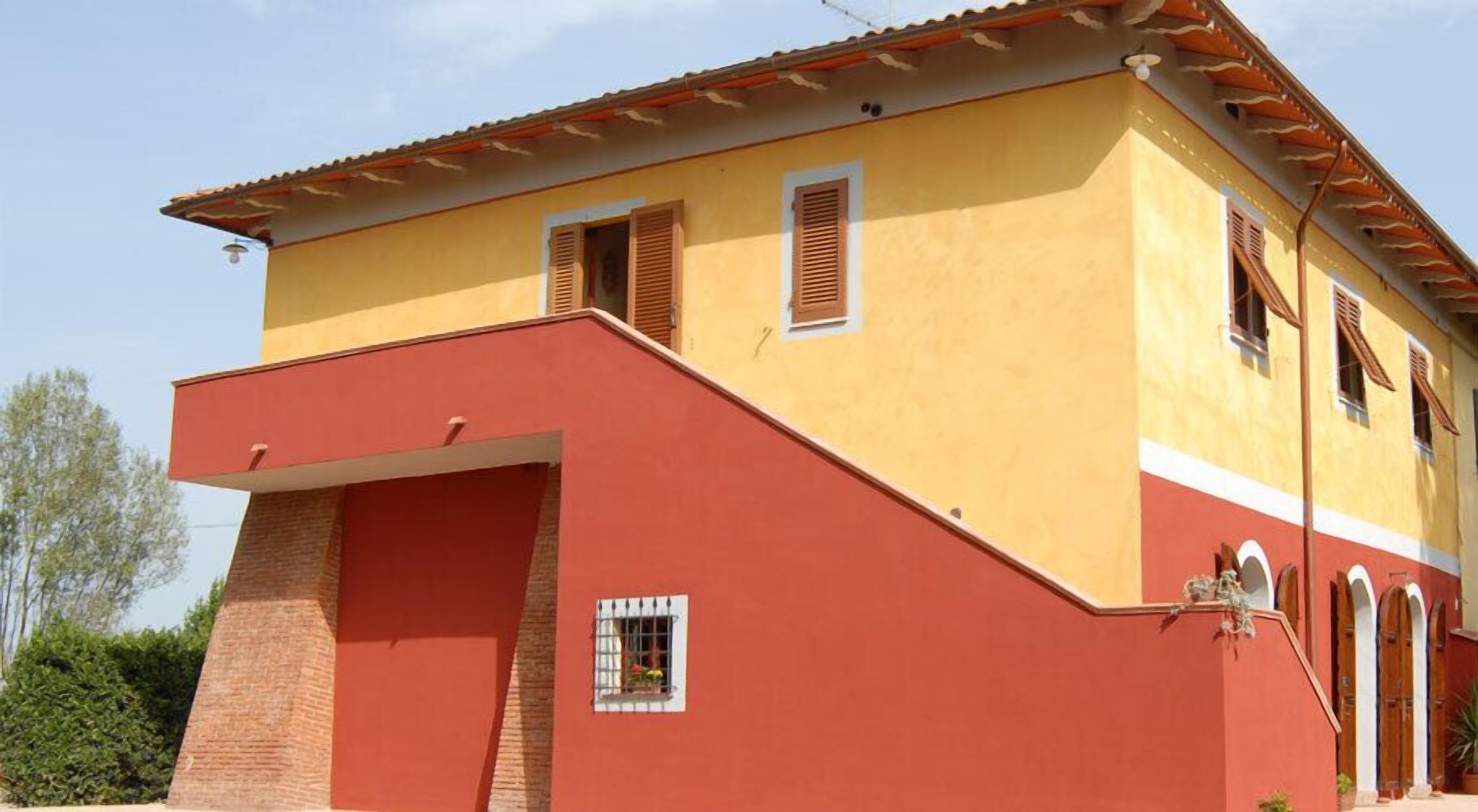 Un edificio di due piani con facciata gialla e dettagli rossi, dotato di un'ampia porta garage e numerose finestre con persiane.