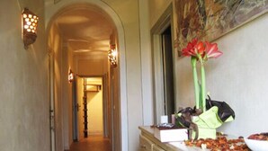 A hallway with a tiled floor, a wooden cabinet with drawers, a vase with flowers, and a painting on the wall. - B&B Il Moscondoro (Montopoli in Val d'Arno)