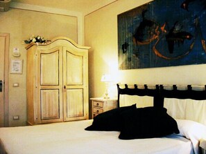 A hotel room with a bed, a wooden wardrobe, a nightstand, and a painting on the wall.