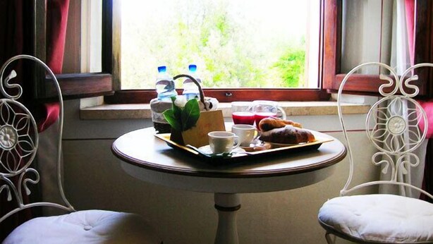 A table with a tray of pastries, a teapot, cups, and water bottles by a window with a view of greenery. - B&B Il Moscondoro (Montopoli in Val d'Arno)