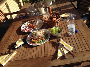 A wooden table with plates of food, a basket of bread, a bowl of grapes, and a bottle of water.
