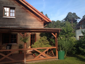 A wooden house with a covered porch, brick walls, and a garden. - Haus Stoertebeker Appartements - Hotel Garni (Lubmin)