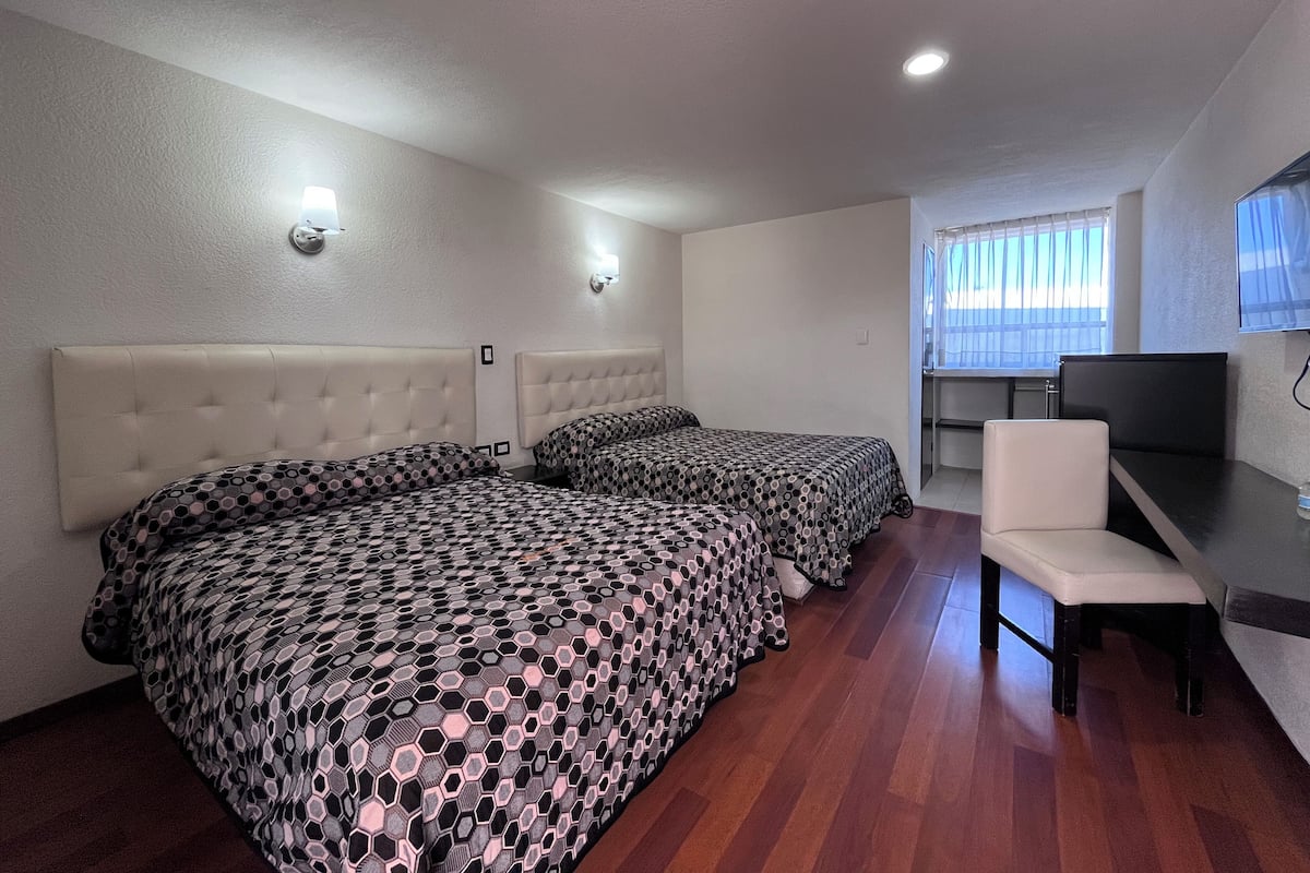 A hotel room with two beds, a desk, a chair, and a TV.